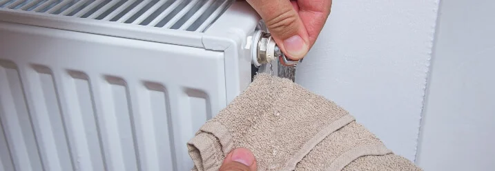 Person hält einen Lappen an ein undichtes Heizkörperventil.